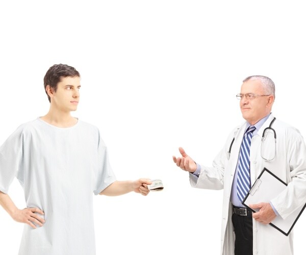 male patient in hospital gown handing over cash to doctor