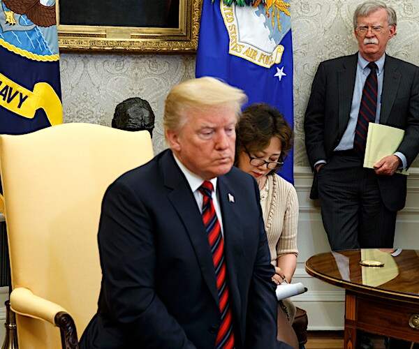 john bolton stands in the background as president donald trump sits with his head down in the oval office