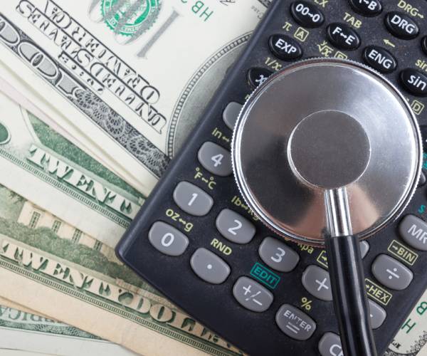 stethoscope lying on a calculator and a spread of twenty dollar bills