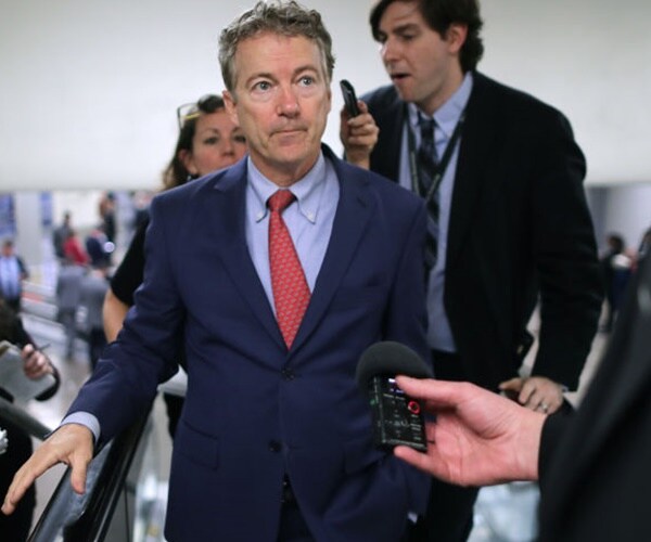 rand paul rides on an escalator with reporters all around him