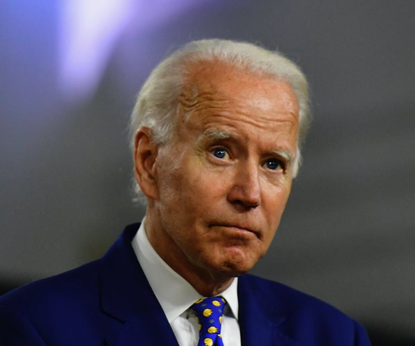 former vice president joe biden gestures with his hand raised in blue suit, blue and yellow tie and white dress shirt