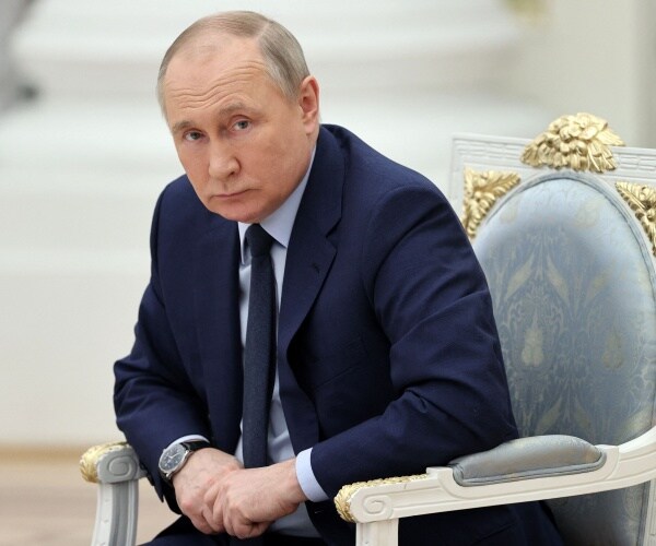 vladimir putin sits in a chair