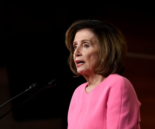 nancy pelosi speaking into a mic wearing a pink dress