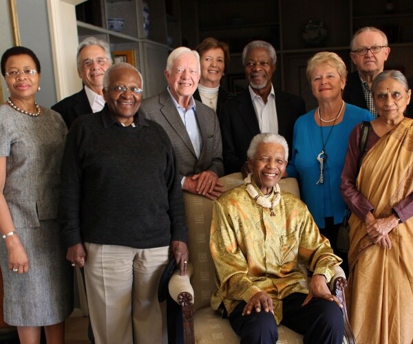 nelson mandela sits down in a chair with world leaders standing around him