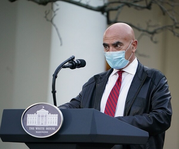 moncef slaoui stands behind podium wearing mask