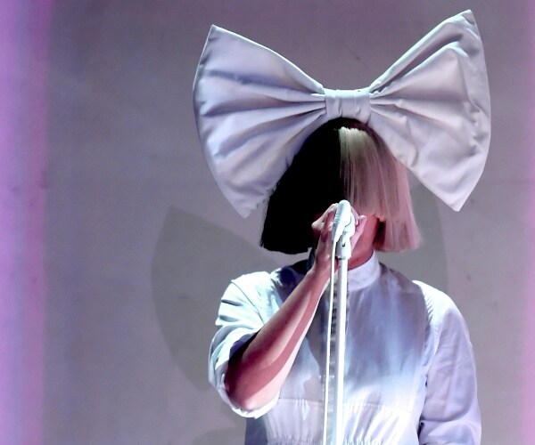 sia wearing a white dress and covering her face with her hair