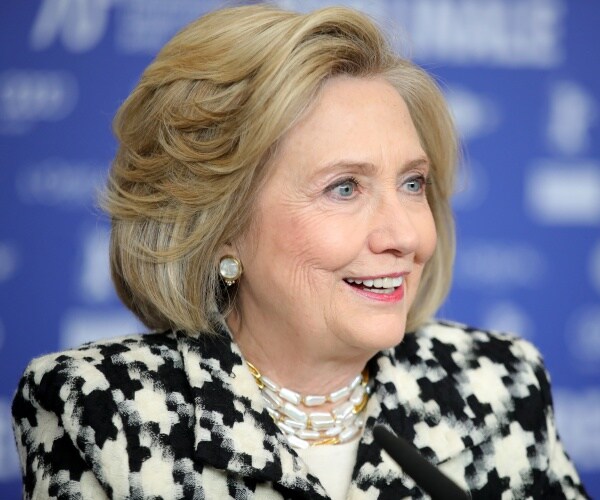 clinton in a black white and gray puzzle piece patterned coat and white top with a beaded necklace