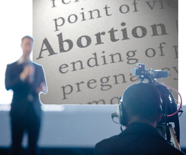 a news reporter in front of a television camera with the dictionary definition of abortion behind him on the screen