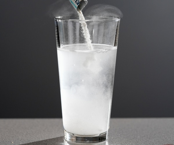 person pouring electrolyte powder into a glass of water
