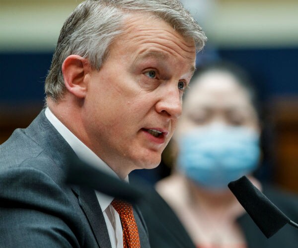 dr. rick bright testifies on capitol hill in a grey suit, white dress shirt and orange tie