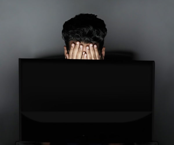 man behind computer with head in hands in dark office