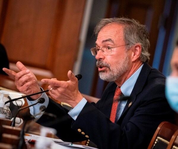 harris in a suit and red tie speaking at a hearing