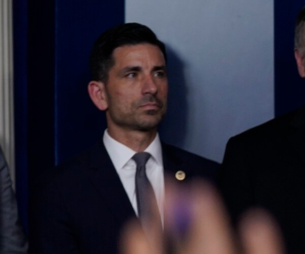 chad wolf stands against a wall and listens to president donald trump speak.