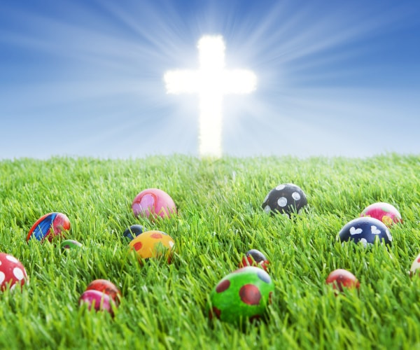 colorful easter eggs lying on the grass with a bright cross in the background
