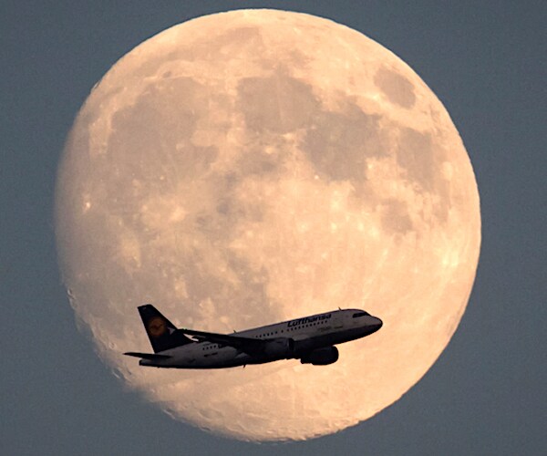 a plane flies in front of a large rising full moon