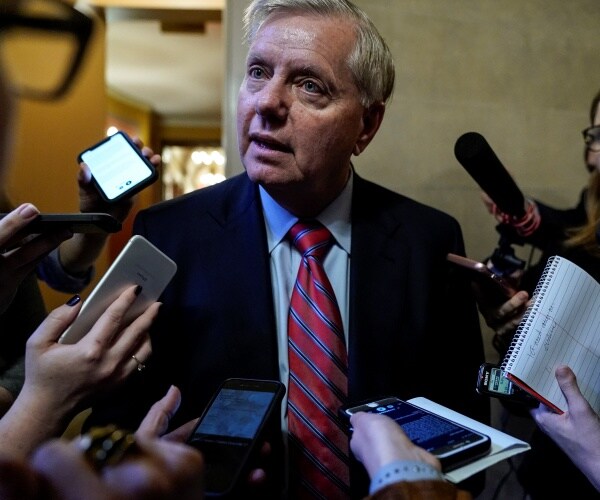 lindsey graham in a red striped tie with many smart phones being pointed to him by reporters