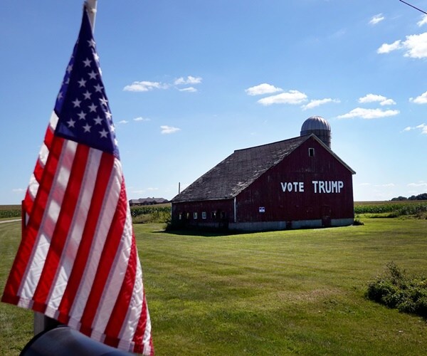 a barn is painted with vote trump and a flag stands nearby.