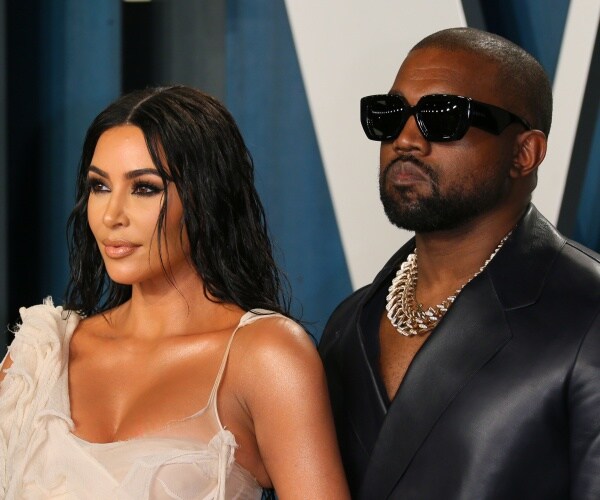 kim in a cream colored dress and kanye in a black suit and sunglasses