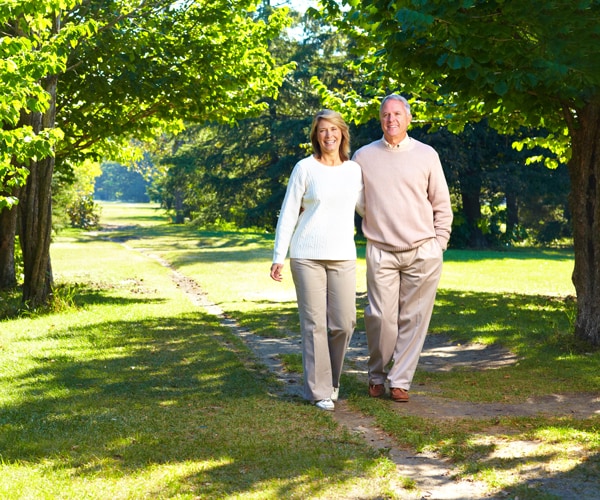 two senior citizens walking together in a park and smiling