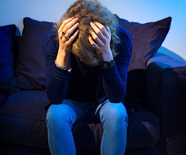 a woman sits on a couch and buries her head in her hands