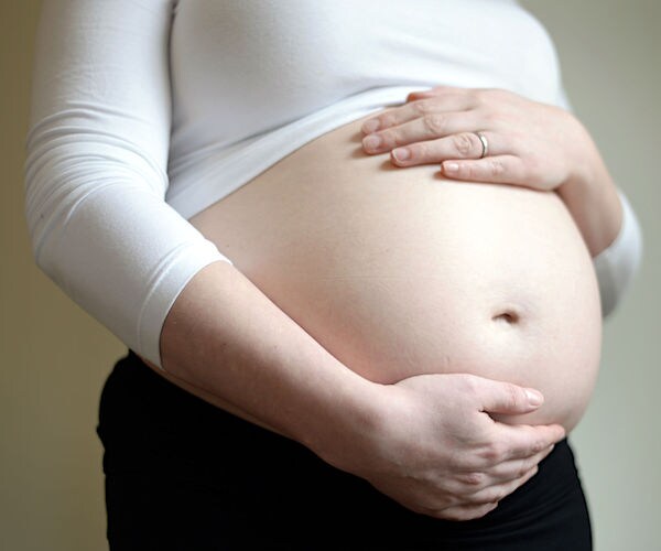 a pregnant woman holds her bare, protruding belly with both hands and arms wrapped around it
