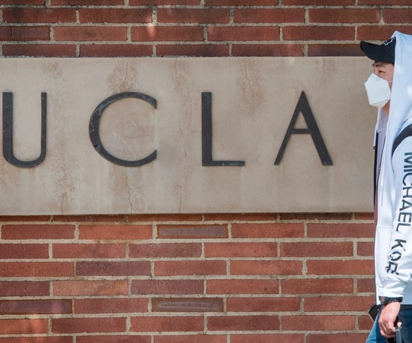 a student walks past a ucla sign wearing a mask