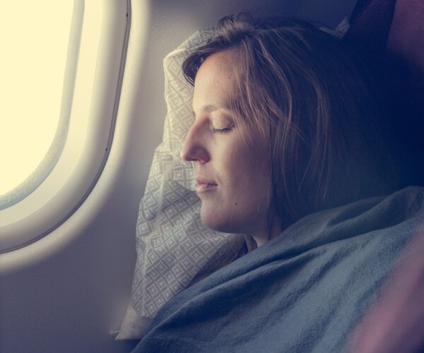 woman with blanket on, sleeping by window of airplane