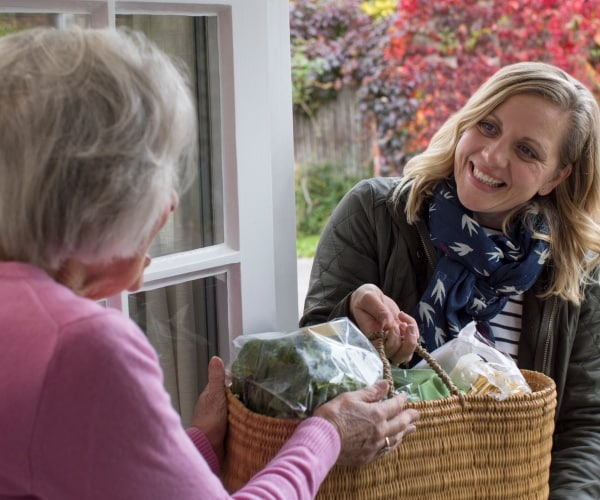 woman bringing groceries to her older neighbor