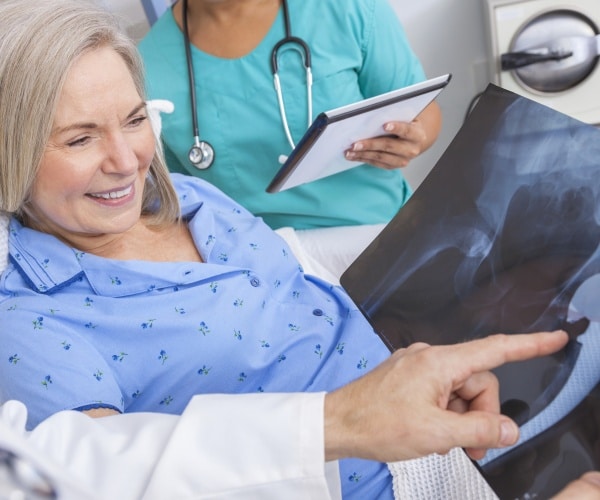 woman in hospital smiling, looking at hip replacement x-ray with doctor