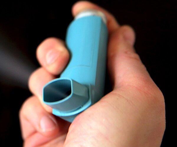 a man's right hand holds a blue asthma inhaler