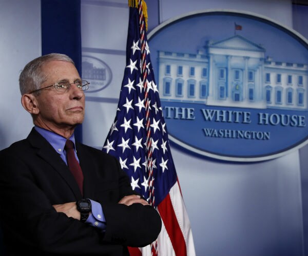 dr. anthony fauci is shown with his arms folded in the white house at a coronavirus briefing