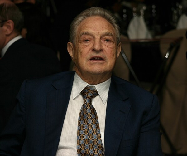 George Soros in blue jacket, white shirt blue and gold tie looking ahead into camera