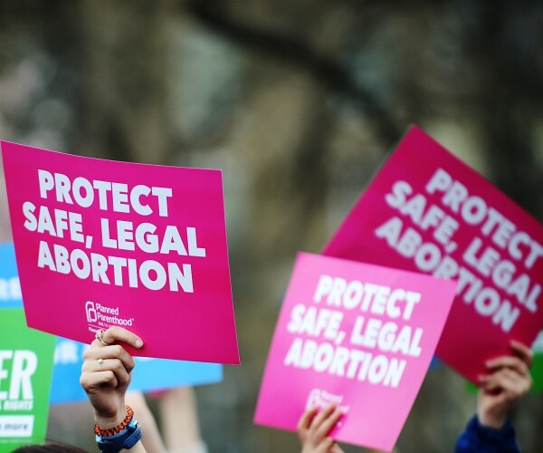hands holding signs that say protect safe legal abortion