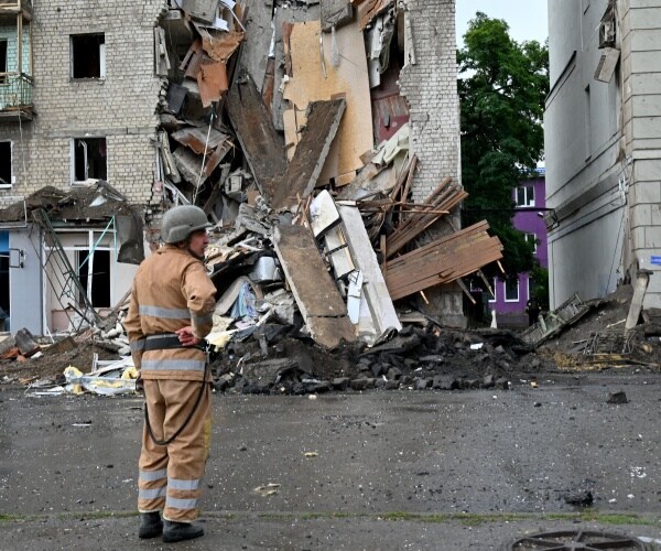 a rescue worker stands next to a building partially destroyed in a missile strike