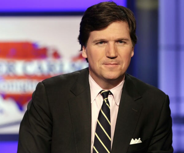 tucker carlson is shown in suit, dress shirt and black and yellow necktie on set