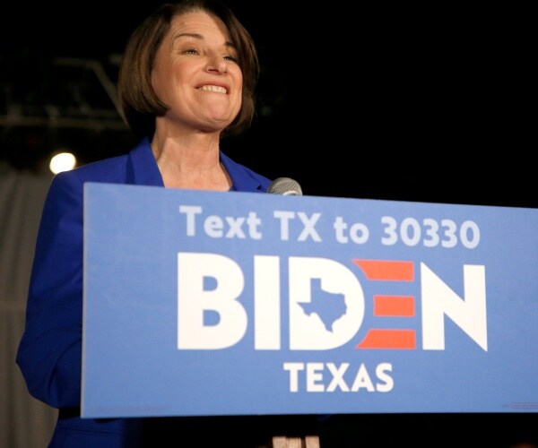 amy klobuchar in a blue suit speaks at a podium at a joe biden campaign event in texas