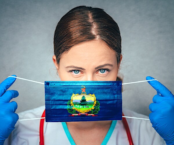 a beautiful nurse dons a blue facemask with the vermont state shield on it