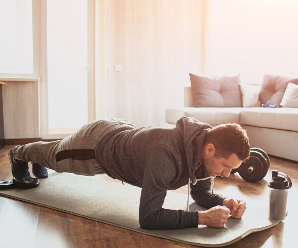 man wearing a gray sweatshirt and sweatpants doing a plank on an exercise mat