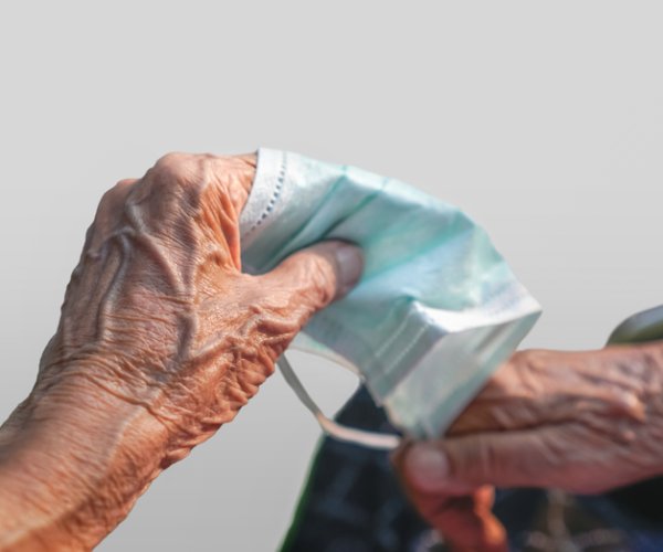 an elderly person clasps a virus mask