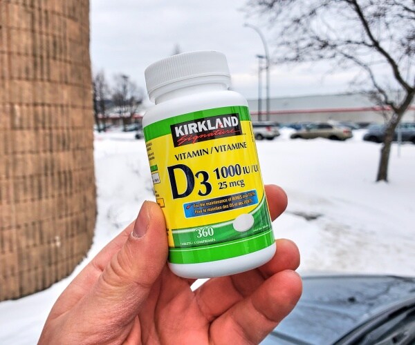 person holding a vitamin d tablet bottle outside with snow in the background