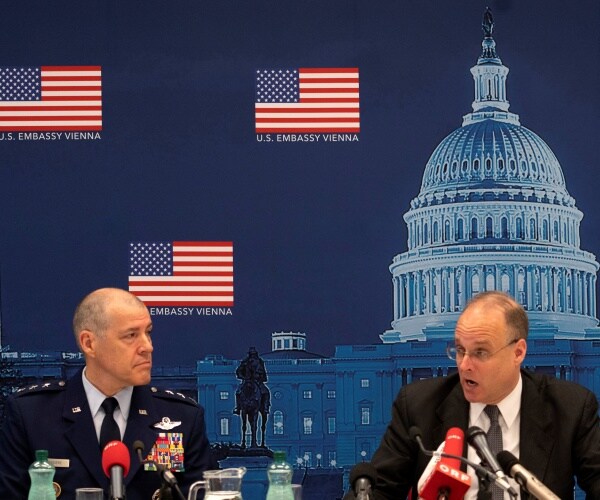 billingslea and bussiere in suits speak at a conference in front of a background with the us capitol