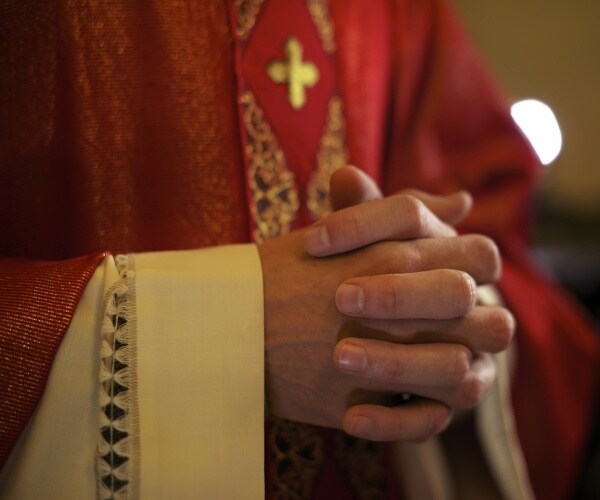 catholic priest on altar praying with hands joined during mass service in church