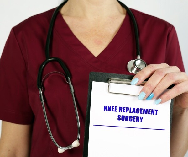 healthcare worker in scrubs holding clipboard with "knee replacement" as heading