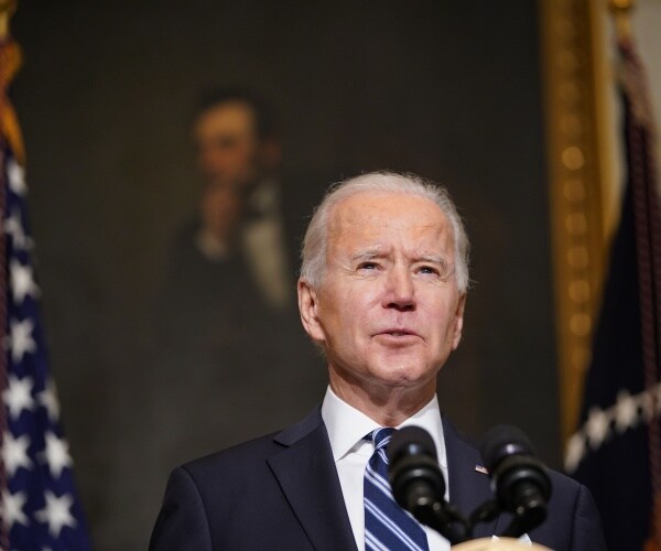 biden in a suit and blue and white striped tie in front of a painting