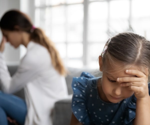upset anxious young girl in foreground, mom in background looking upset and anxious too