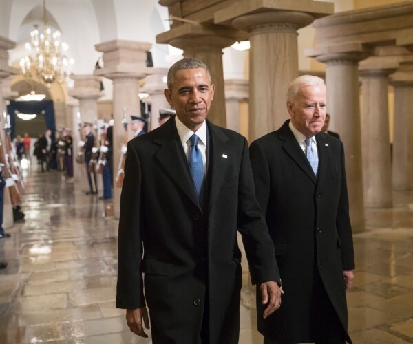 obama and biden walk together in the capitol in black coats