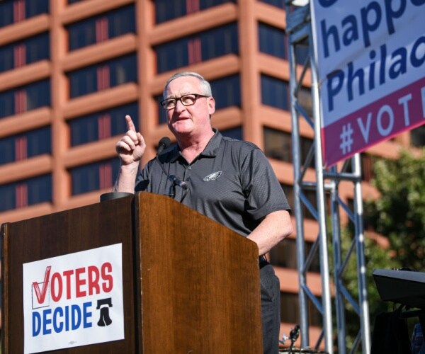 mayor in dark shirt gestures behind lectern with voters decide sign