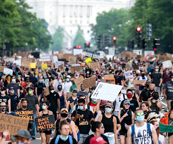 a crowd protesting police brutality marches to defund the police
