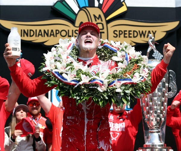 the race winner holds his arms up and shouts while holding a jug of milk in one hand