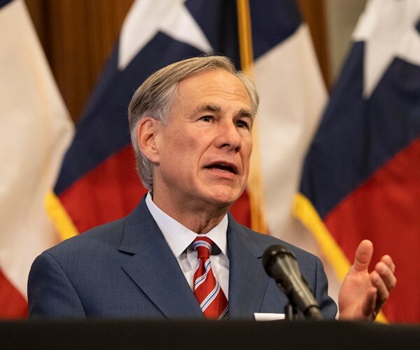 gov. abbott is in front of texas flags announcing the opening of the state.